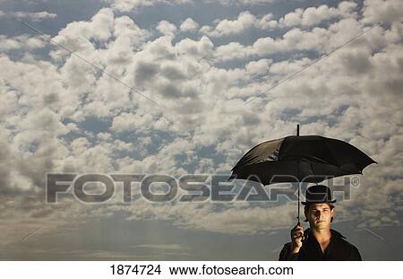 a man wearing a top hat and holding an umbrella under a sky filled with clouds View Large Photo Image Picture - a man wearing a top hat and holding an umbrella under a sky filled with clouds. Fotosearch