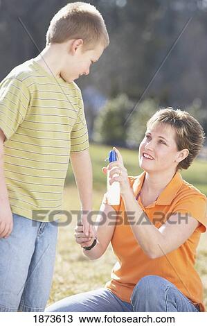 Stock Image - a mother spraying insect repellent on her son. Fotosearch