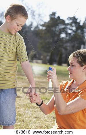 Stock Photograph - a mother spraying insect repellent on her son's arm. Fotosearch