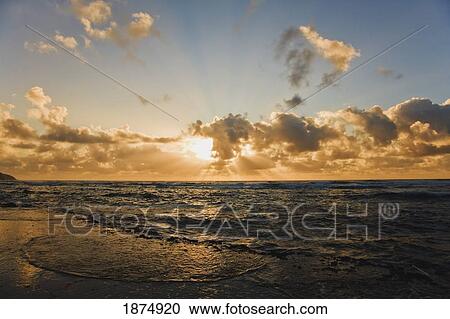 Stock Image - a sunburst through the clouds over the water. Fotosearch