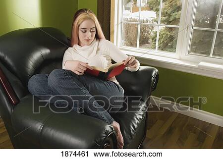 Stock Image - a woman sitting in a chair and reading a book. Fotosearch