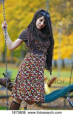 Stock Photo - a young woman standing on a swing at a playground in autumn. Fotosearch