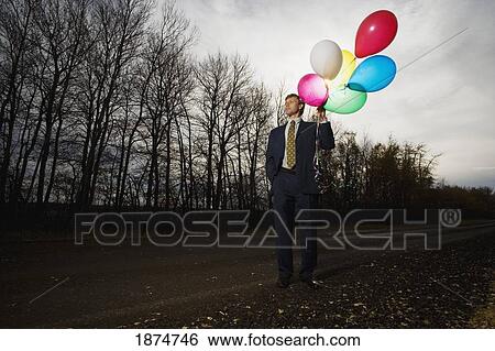 Stock Photograph - alberta, canada; a businessman standing on the side of the road holding balloons. Fotosearch