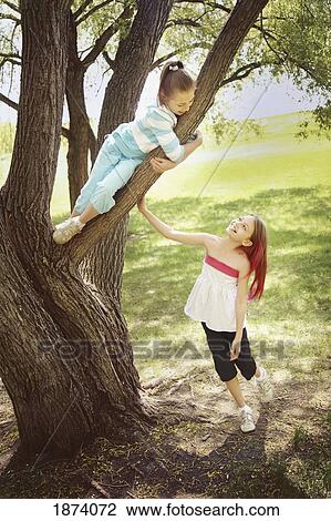 Stock Image - edmonton, alberta, canada; a girl talking to her friend who is sitting in a tree. Fotosearch