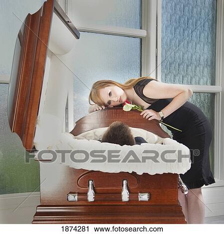 Stock Image - edmonton, alberta, canada; a young woman holds a rose and lays her head on the coffin of a deceased loved one. Fotosearch