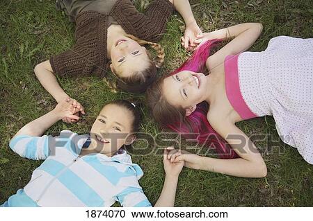 Stock Image - edmonton, alberta, canada; three girls laying on the grass holding hands in the shape of a star. Fotosearch