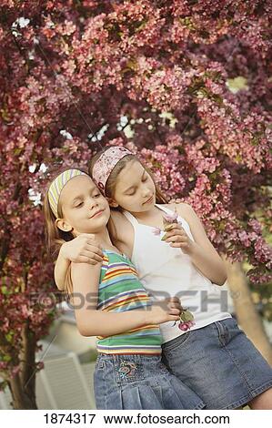 Stock Photo - edmonton, alberta, canada; two girls holding flowers under a blossoming tree. Fotosearch
