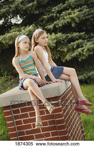 Stock Photography - edmonton, alberta, canada; two girls sitting on a brick pillar. Fotosearch