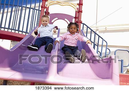 Picture - fort lauderdale, florida, united states of america; two young children going down the slide at the playground. Fotosearch