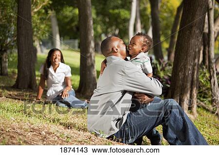 Stock Image - fort lauderdale, florida, united states of america; a father and young son hug while the mother watches. Fotosearch