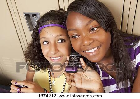 Stock Image - fort lauderdale, florida, united states of america; two teenage girls using a cell phone while sitting in a school hallway. Fotosearch