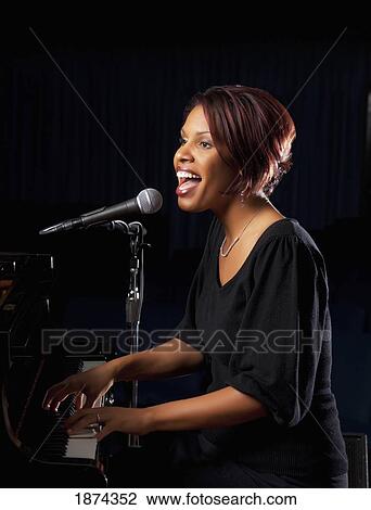 Stock Image - fort lauderdale, florida, united states of america; a woman playing the piano and singing into a microphone. Fotosearch