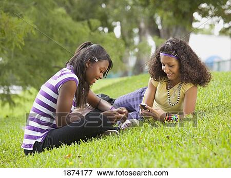 Stock Photo - fort lauderdale, florida, united states of america; two teenage girls using their cell phones while laying on the grass. Fotosearch