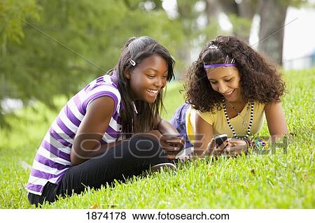 Stock Photo - fort lauderdale, florida, united states of america; two teenage girls using their cell phones while laying on the grass. Fotosearch