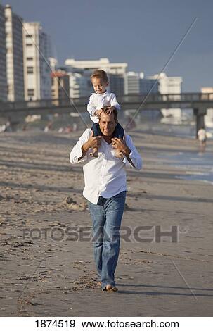 Stock Photo - fort lauderdale, florida, united states of america; a father walking on the beach with his son on his shoulders. Fotosearch