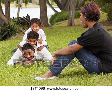 Stock Photograph - fort lauderdale, florida, united states of america; sons piling on their father's back while their mother watches. Fotosearch