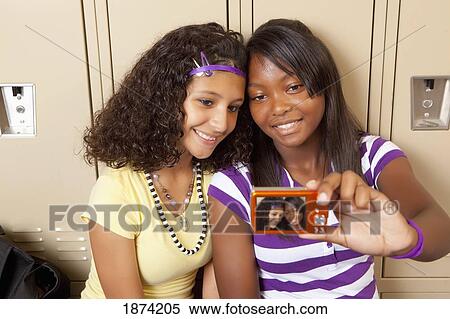 Stock Photography - fort lauderdale, florida, united states of america; two teenage girls sitting in a school hallway taking a picture of themselves. Fotosearch