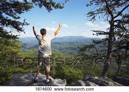 Stock Image - knoxville, tennessee, united states of america; a teenage boy stands with arms raised while overlooking the mountains. Fotosearch