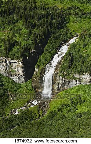 Stock Image - montana, united states of america; a large waterfall flows through summer vegetation near logan pass at glacier national park. Fotosearch