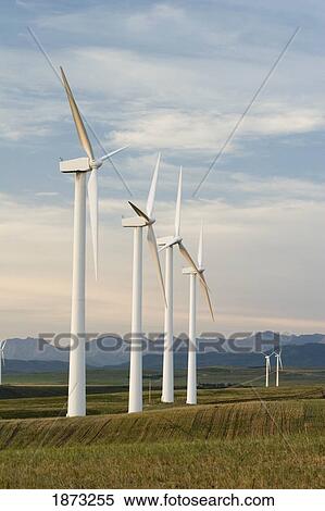 Stock Photography - pincher creek, alberta, canada; wind turbines in a row and mountains in the background. Fotosearch