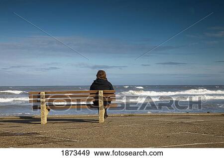 Stock Photo - saltburn, teesside, england; a woman sitting on a bench and watching the waves on the water. Fotosearch