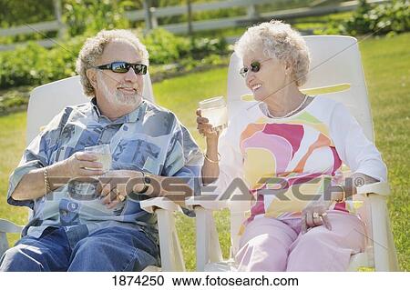 Stock Image - sherwood park, alberta, canada; a couple sitting in lawn chairs enjoying drinks. Fotosearch