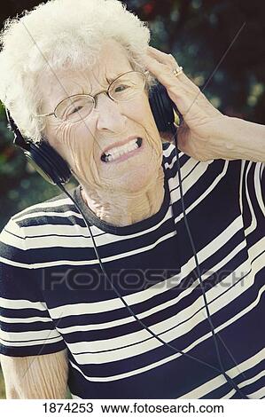 Stock Image - sherwood park, alberta, canada; a senior woman cringing at the music coming through her headphones. Fotosearch