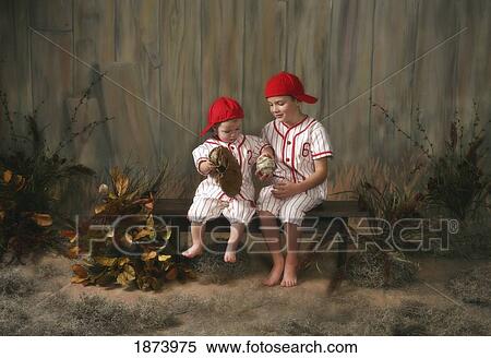 two boys sitting on a bench wearing baseball uniforms View Large Photo Image Stock Photography - two boys sitting on a bench wearing baseball uniforms. Fotosearch