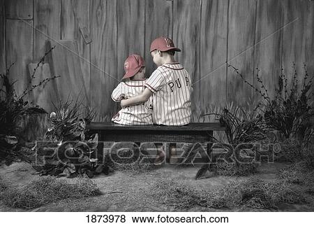 two boys wearing baseball uniforms and sitting on a bench together View Large Photo Image Stock Photo - two boys wearing baseball uniforms and sitting on a bench together. Fotosearch
