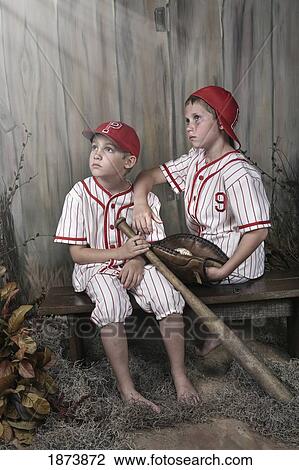 two boys wearing baseball uniforms sitting on a bench View Large Photo Image Stock Image - two boys wearing baseball uniforms sitting on a bench. Fotosearch