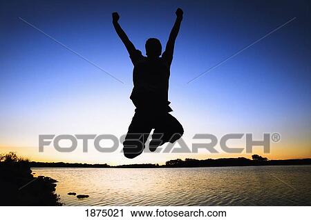 Stock Image - willmar, minnesota, united states of america; silhouette of a person jumping in the air by the water at sunset. Fotosearch