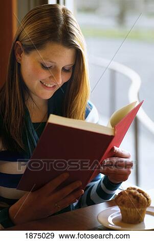 willmar, minnesota, united states of america; a girl sits with her muffin at a restaurant table reading a book View Large Photo Image Stock Photo - willmar, minnesota, united states of america; a girl sits with her muffin at a restaurant table reading a book. Fotosearch