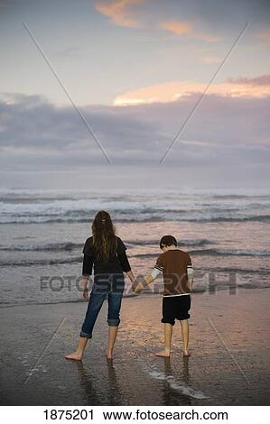 Stock Image - A mother and son hold hands on a beach looking out at the water. Fotosearch