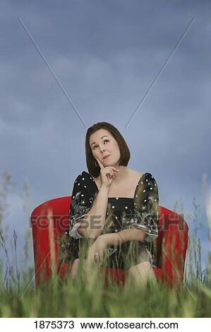a woman sitting in a red chair in a field in a thinking pose View Large Photo Image Stock Image - a woman sitting in a red chair in a field in a thinking pose. Fotosearch