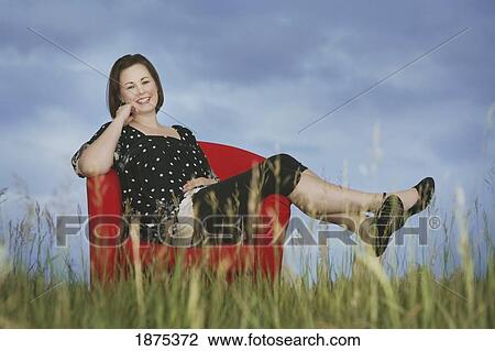 a woman sitting in a red chair in the middle of a field View Large Photo Image Stock Image - a woman sitting in a red chair in the middle of a field. Fotosearch