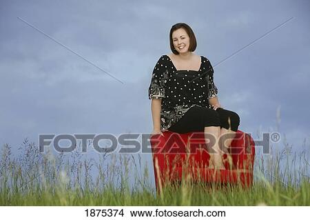 Picture - a woman sitting on a red chair in a field. Fotosearch