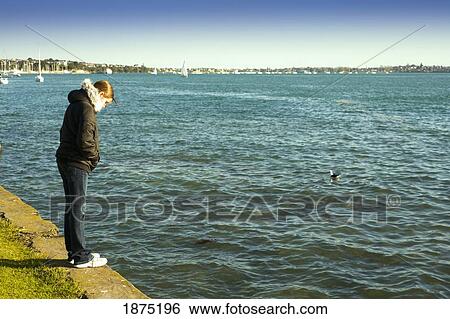 a woman standing on the retaining wall at the water's edge View Large Photo Image Stock Photograph - a woman standing on the retaining wall at the water's edge. Fotosearch