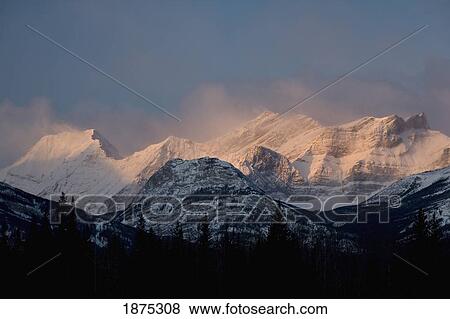 Stock Photo - alberta, canada; fog around the snow covered mountain range at sunrise in kananaskis country. Fotosearch