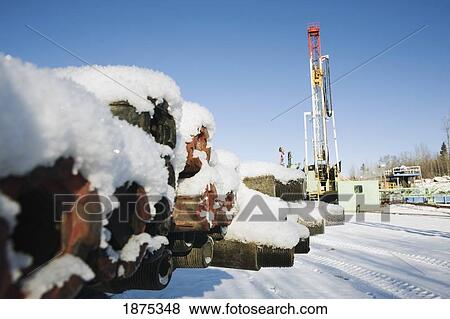Stock Photo - edson, alberta, canada; snow covered drilling pipes with a rig in the background. Fotosearch