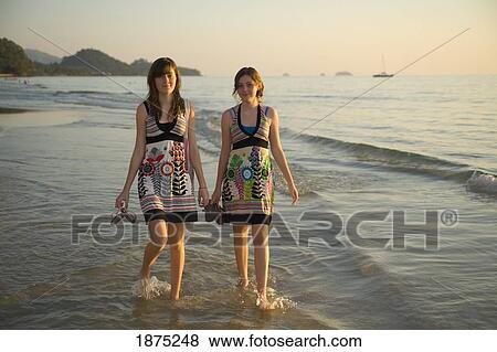 Stock Photo - koh chang, thailand; two girls walking barefoot in the shallow water along the beach. Fotosearch