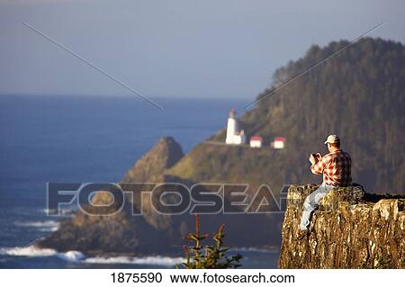 oregon, united states of america; a man sitting on a cliff and taking pictures of the heceta head lighthouse along the coast of the pacific ocean View Large Photo Image Stock Image - oregon, united states of america; a man sitting on a cliff and taking pictures of the heceta head lighthouse along the coast of the pacific ocean. Fotosearch