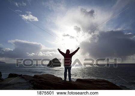 oregon, united states of america; silhouette of a person lifting their hands standing at cape kiwanda cliffs with a view of haystack rock View Large Photo Image Stock Image - oregon, united states of america; silhouette of a person lifting their hands standing at cape kiwanda cliffs with a view of haystack rock. Fotosearch