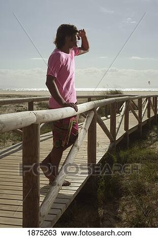 Stock Image - tarifa, costa de la luz, cadiz, andalucia, spain; a man stands at the railing of a boardwalk leading out to dos mares beach in front of hotel dos mares. Fotosearch