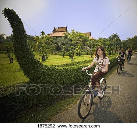 Stock Image - thailand; two girls and a woman riding their bikes down the road. Fotosearch