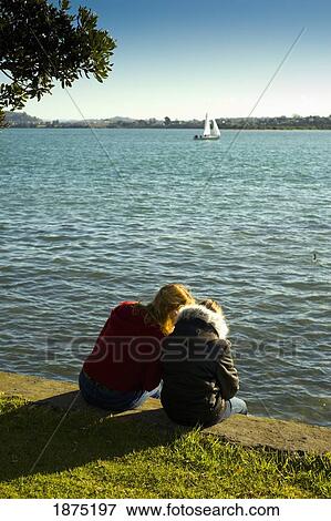 Stock Photo - two girls sitting on a retaining wall at the water's edge. Fotosearch