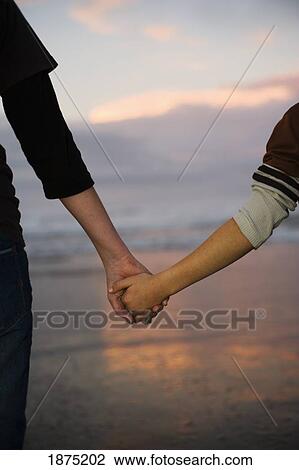 Stock Image - Two people holding hands on the beach. Fotosearch