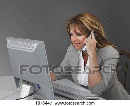 Jordan, Ontario, Canada; A Businesswoman Working At A Desk With A Computer And Talking On The Phone View Large Photo Image Stock Photo - Jordan, Ontario, Canada; A Businesswoman Working At A Desk With A Computer And Talking On The Phone. Fotosearch