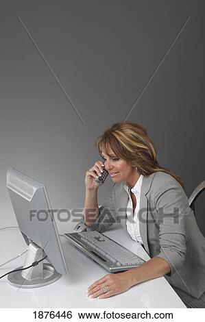 Jordan, Ontario, Canada; A Businesswoman Working At A Desk With A Computer And Talking On The Phone View Large Photo Image Stock Photograph - Jordan, Ontario, Canada; A Businesswoman Working At A Desk With A Computer And Talking On The Phone. Fotosearch