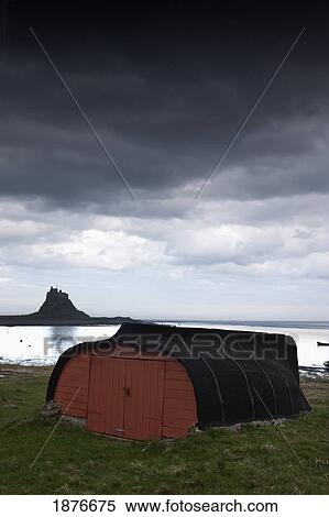 Stock Photography - Lindisfarne, Northumberland, England; A Red Wooden Building With A View Of Lindisfarne Castle. Fotosearch