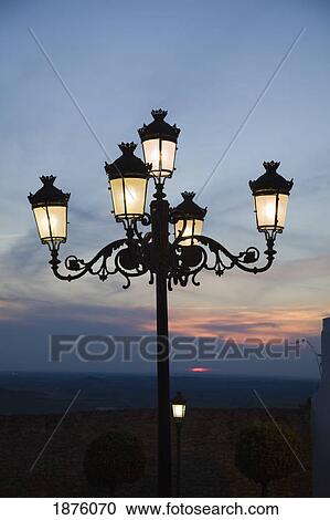 Stock Image - Medina Sidonia, Andalusia, Spain; A Light Post With 5 Lamps On It Illuminated At Night. Fotosearch